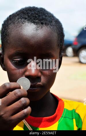 Un garçon burkinabé qui détient une pièce de 100 francs d'Afrique de l'Ouest. Banque D'Images