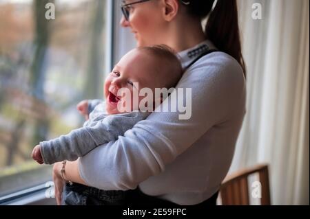 Mère debout près de la fenêtre et tenant un petit bébé mignon Banque D'Images