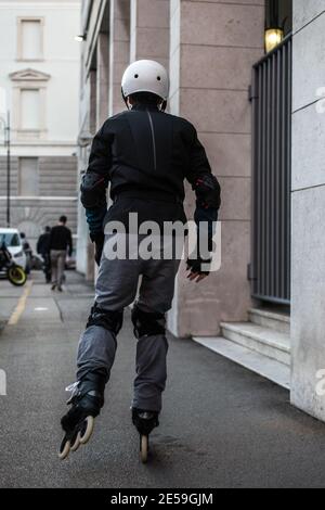 Vue arrière d'un homme portant un casque et des genouillères sur les patins à roues alignées en plein air dans une rue urbaine Banque D'Images