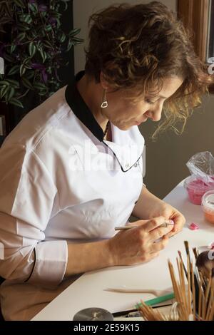 Processus de décoration de gâteau. Baker utilise des outils pour sculpter des motifs fondants : art comestible, design de gâteau, décoration de gâteau. Mise au point sélective des outils frontaux et de la main Banque D'Images