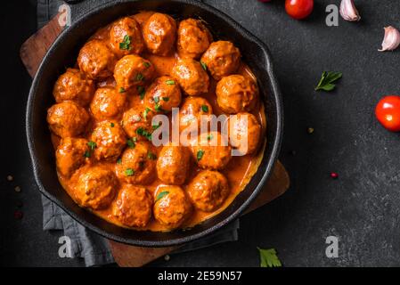 Boulettes de viande faites maison à la sauce tomate en gros plan. Boulettes de viande de bœuf dans un moule en fonte sur fond noir. Banque D'Images