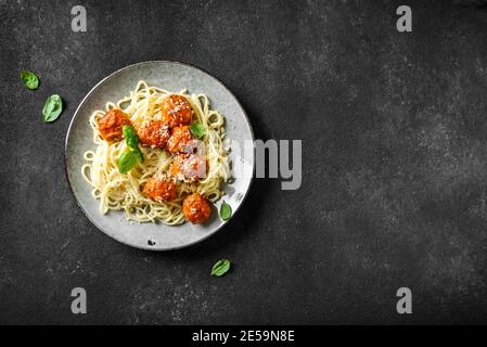 Pâtes spaghetti aux boulettes de viande, sauce tomate, fromage râpé et basilic frais - pâtes italiennes maison saines sur fond noir, vue du dessus, espace copie Banque D'Images