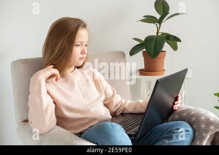 Écolière utilisant un ordinateur portable sur un fauteuil. École à domicile, éducation en ligne, éducation à domicile, concept de quarantaine - image Banque D'Images