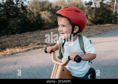 Enfant heureux portant un casque de vélo. Un jeune garçon souriant qui fait du vélo d'équilibre un soir d'été. Banque D'Images