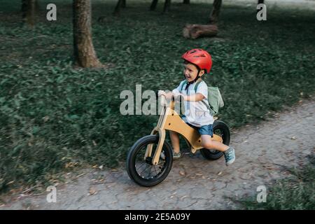 Enfant heureux portant un casque de vélo. Un jeune garçon souriant qui fait du vélo d'équilibre dans un parc en soirée d'été. Banque D'Images