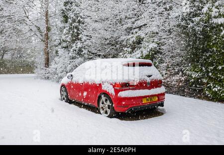 Une voiture rouge Volkswagen Golf GTI garée dans un périurbain couvert de neige pendant une forte chute de neige en hiver : Woking, Surrey, sud-est de l'Angleterre Banque D'Images