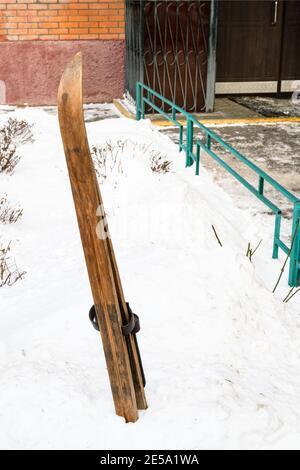 vieux skis en bois en déneigement près de l'entrée de la maison de ville le jour d'hiver Banque D'Images