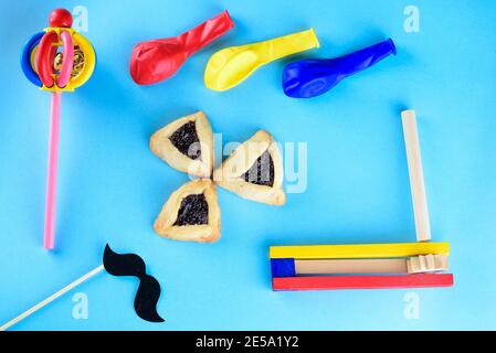 Biscuits Hamantaschen ou oreilles de hamans, les bruyères de bois colorés, drôle de papier masque de moustache sur un bâton et des ballons pour la célébration de Purim fête juive carnaval sur fond bleu.vue du dessus.Flat Lay. Banque D'Images