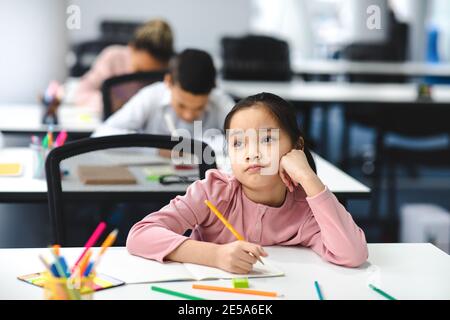 Une jeune fille d'école asiatique ennuyeuse assise au bureau dans la salle de classe Banque D'Images