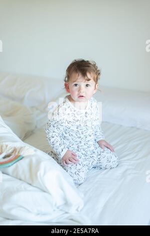 Petite fille portant un pyjama jouant dans le lit Banque D'Images