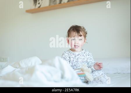 Petite fille portant un pyjama jouant dans le lit Banque D'Images