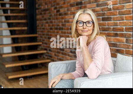 Un portrait d'affaires d'une charmante femme d'âge moyen portant des lunettes regarde l'appareil photo, une dame confiante est assise à un fauteuil dans un espace de bureau, psychologue Banque D'Images