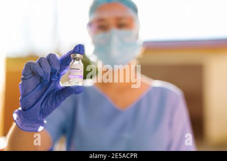 Portrait flou d'un professionnel de santé tenant une ampoule de vaccin Covid 19 sur fond de soleil éclatant. Le concept de combat Banque D'Images
