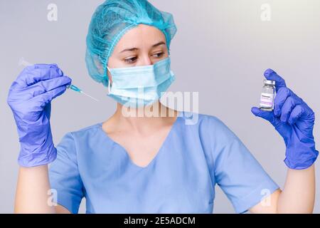 Jeune femme médecin concentrée dans un masque médical et stérile gants tient une seringue dans ses mains et regarde une ampoule avec un vaccin covid 19 Banque D'Images