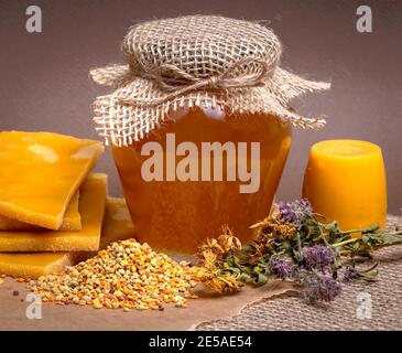 Miel dans un pot avec un balancier de miel, pollen d'abeille ciré et fleurs séchées sur fond de bois vintage Banque D'Images