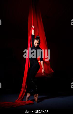 Une femme est engagée dans des acrobaties aériennes sur fond sombre. Gymnastique sportive faire des exercices sur toile Banque D'Images