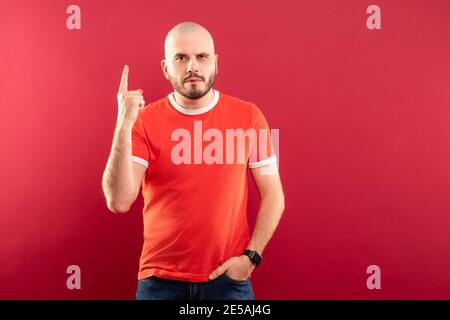 Un homme d'âge moyen avec une barbe dans un T-shirt rouge sur fond rouge pointe joyeusement vers le haut. Isolé Banque D'Images