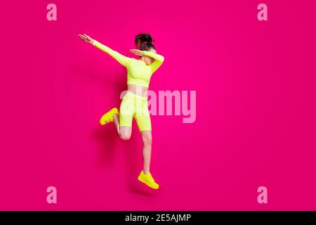 Photo de la taille du corps pleine longueur de jumping sportswoman porter jaune baskets sportswear affichant un battage publicitaire isolé sur fond rose vif Banque D'Images