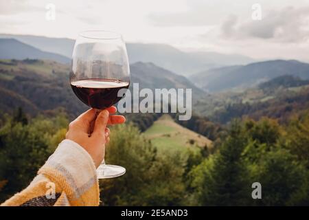Main de femme tenant un verre de vin rouge avec vue sur la montagne. Banque D'Images