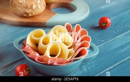 Salami italien, saucisse et fromage dans un bol en céramique. Tomates cerises. Planche à découper avec pains à grains entiers.planches en bois turquoise. Banque D'Images