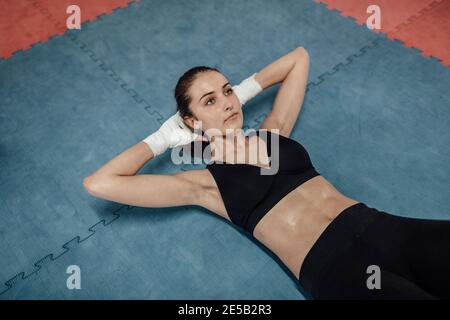 Jeune femme athlétique s'assoir dans une salle de sport. Portrait d'une athlète féminine dans un soutien-gorge de sport allongé sur un tapis de fitness et d'exercice. Banque D'Images