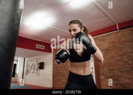 Portrait d'une boxeuse de boxe qui a poinçonné un sac de boxe. Une femme portant des gants de boxe s'est mise à l'entraînement lors d'un cours de kickboxing. Banque D'Images