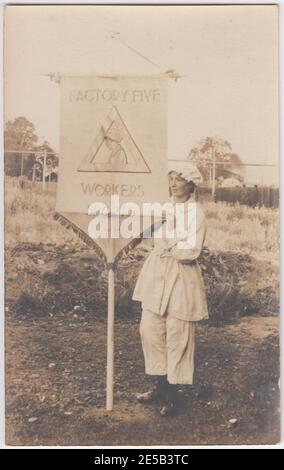 Ouvrier de munitions de la première Guerre mondiale tenant une bannière pour promouvoir Factory Five Workers Sports, la bannière inclut une image agrandie de l'insigne des travailleurs de munitions. La femme est habillée en vêtements de travail, y compris un pantalon et des bottes substantielles Banque D'Images