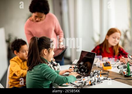 Groupe d'enfants heureux avec leur science féminine afro-américaine professeur avec des jouets électriques de programmation d'ordinateur portable et des robots à la robotique salle de classe Banque D'Images