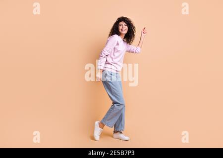 Pleine photo de profil de fille optimiste curly vêtements de danse pull jeans sneakers isolées sur fond de couleur pêche Banque D'Images