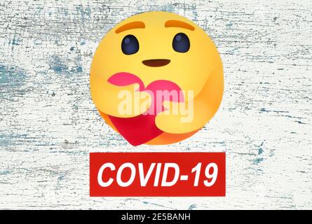 Kiev, Ukraine - 25 août 2020: Facebook New Care empathique réaction d'Emoji avec Covid-19 label sur fond de bois. Facebook ajoute un « hug reacti » Banque D'Images