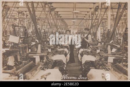 Hangar à tissage dans un moulin à coton du Lancashire, Bury.Trois garçons travaillent parmi les machines de l'usine, une femme est à l'arrière-plan, au début du XXe siècle Banque D'Images
