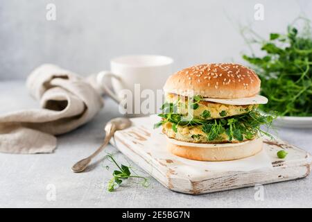 Hamburger végétarien sain avec œufs et pousses de pois et graines microvertes, salade fraîche, tranches de concombre sur une planche à découper en bois sur fond clair. Sél Banque D'Images