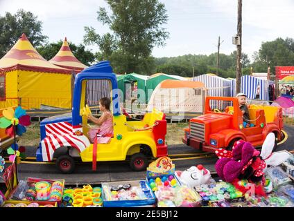 Les enfants sont à bord de voitures à carrousel dans l'aire de jeux lors d'une journée d'été lors du festival international annuel de musique et d'artisanat World of Siberia. Banque D'Images