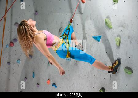 Jeune femme Climber se détendant sur le Belay dans la salle d'escalade. Sport extrême et escalade en intérieur Banque D'Images