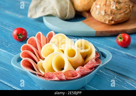 Salami italien, saucisse et fromage dans un bol en céramique. Tomates cerises. Planche à découper avec pains à grains entiers.planches en bois Turquoise, bois Banque D'Images