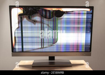 Moniteur LED d'ordinateur sur un bureau avec une grande fissure et des lignes colorées qui s'affichent à l'écran Banque D'Images