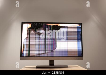 Moniteur LED d'ordinateur sur un bureau avec une grande fissure et des lignes colorées qui s'affichent à l'écran Banque D'Images