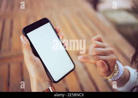 Gros plan sur une femme d'âge moyen assise à la table à l'aide de l'application pour smartphone sur la terrasse. Banque D'Images