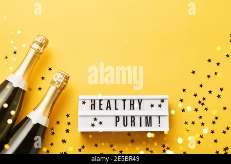 Healthy Purim écrit dans une visionneuse et deux bouteilles de champagne sur fond jaune. Plat de Purim Carnaval Banque D'Images