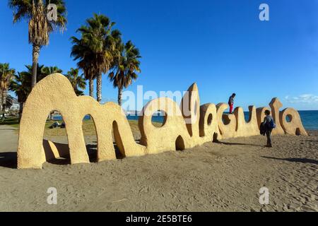 Emblématique signe de sculpture de sable de Malagueta sur la plage de Malaga, Andalousie, Espagne, avec des palmiers et la mer bleue au coucher du soleil. Banque D'Images