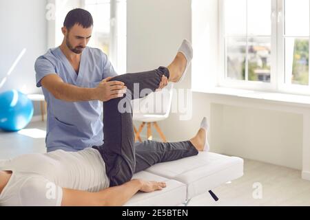 Homme professionnel chiropraticien en bleu uniforme fixation et pose couché homme patients jambes articulations Banque D'Images