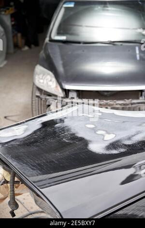 Réparation de la carrosserie, application PuTTY gros plan. Le mécanicien répare la voiture. Travailler après l'accident en travaillant le primaire de ponçage avant de peindre. Banque D'Images