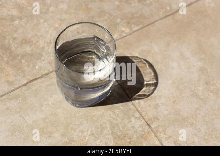 Verre d'eau plate sur la table en plein soleil, ombres longues, sur la table, vue de dessus. Concept de soins de santé, boissons rafraîchissantes d'été, étancher la soif. Haut Banque D'Images