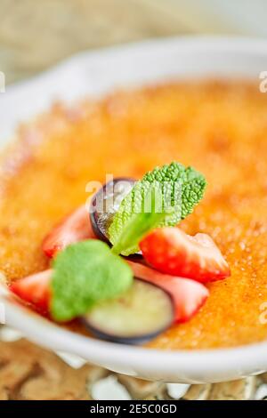 Crème brûlée classique dans un bol en verre. Gros plan sur des glaces appétissantes. Délicieux dessert avec un repas sucré aux raisins et aux fraises, au caramel, à la menthe et Banque D'Images