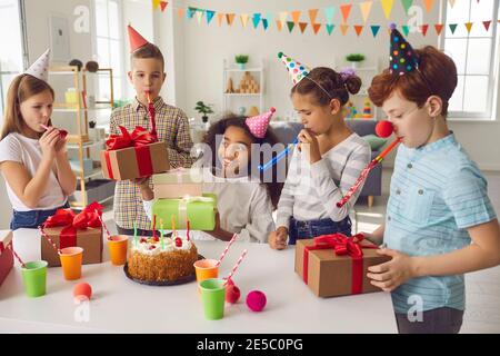 Groupe d'enfants de race mixte souriants avec sifflets décoratifs ayant fête d'anniversaire Banque D'Images