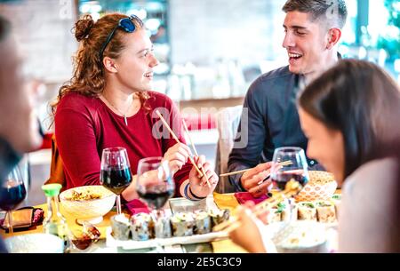 Couple heureux jouant avec des baguettes au bar restaurant sushi - Concept de mode de vie de nourriture avec des gens heureux ayant plaisir à manger ensemble et boire du vin Banque D'Images