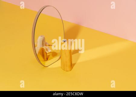 Moitié de banane dans un miroir avec une moitié de pilled. Arrière-plan bicolore. Concept fruit créatif Banque D'Images