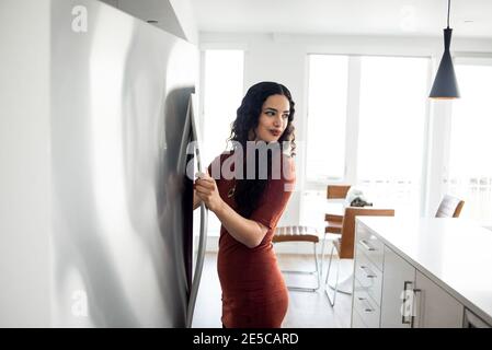 Jeune femme ouvrant quelque chose du frigo et saisissant quelque chose Banque D'Images