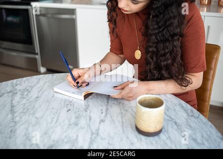 Femme avec de longs cheveux écrivant dans le carnet à la table de cuisine Banque D'Images