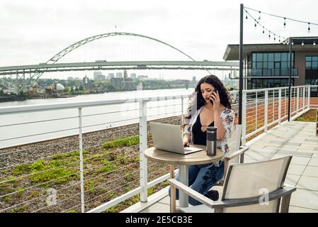 Femme parlant au téléphone et travaillant sur un ordinateur portable à l'extérieur sur le toit Banque D'Images